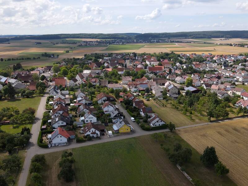 Eine kleine Stadt mit vielen Häusern und Gebäuden liegt eingebettet in eine weite ländliche Landschaft mit Feldern und Wäldern im Hintergrund.